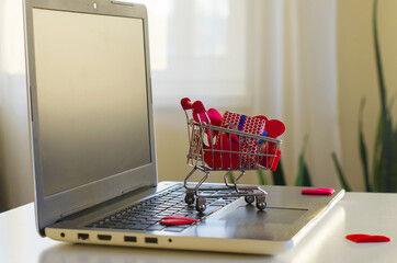 Opened laptop computer on the white  desk, shopping cart, gift box, hearts. Concept of...