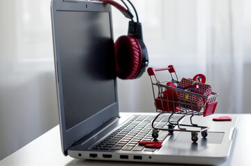 Opened laptop computer on the white  desk, shopping cart, gift box, hearts. Concept of...