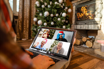 Naklejka na ściany i meble Happy girl in santa hat gereeting friends with christmas in video chat on laptop. Young woman lying under decorated pine tree among gift boxes and packages in home interior with copy space