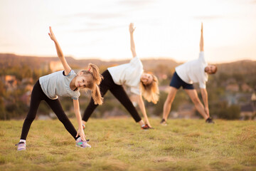 Parents instill sports habits in their child by example, focus on child. Happy sporty family doing stretching exercises, practices yoga outdoor. Mom dad and daughter doing sport exercises