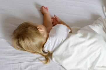 Obraz na płótnie Canvas Faceless toddler girl with blonde hair sleeping on white bed. Rear view of a two year old child girl sleeping a beautiful and comfortable bed