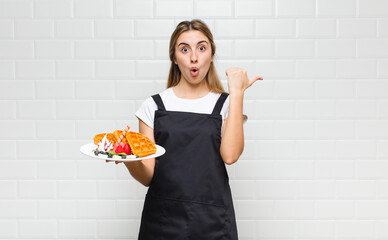 blonde pretty woman looking astonished in disbelief, pointing at object on the side and saying wow,...
