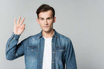Brunette man in denim jacket showing ok gesture isolated on grey