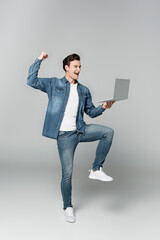 Cheerful man showing yeah gesture while holding laptop on grey background