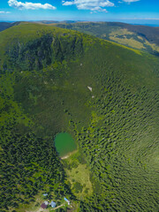 Aerial drone panorama of Iezerul Sureanu glacier lake and one mountain peak. The high altitude mountain side has juniper trees grown on it. Sureanu Mountains, Carpathia, Romania