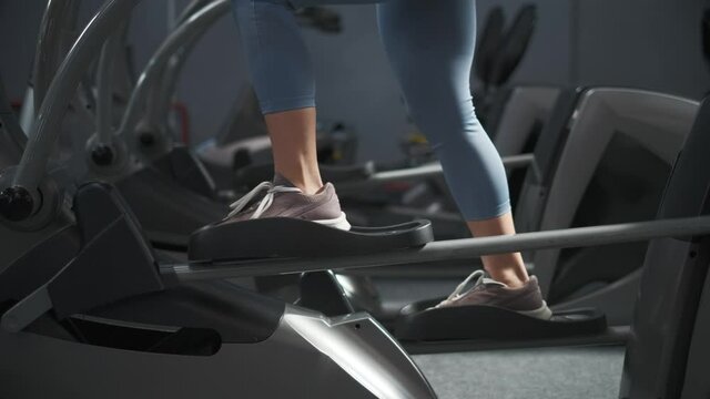 Young woman is working out on stepper in a gym. She is walking on orbitrek for cardio intensity and endurance improvement. Fit woman on cardio stepper. Fitness, body and health concept