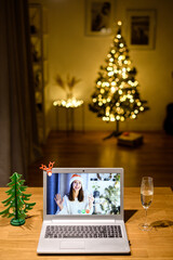 Virtual celebration Christmas eve. A girl in santa hat with a glass of champagne waving hello on the laptop screen. Video call, virtual meeting concept