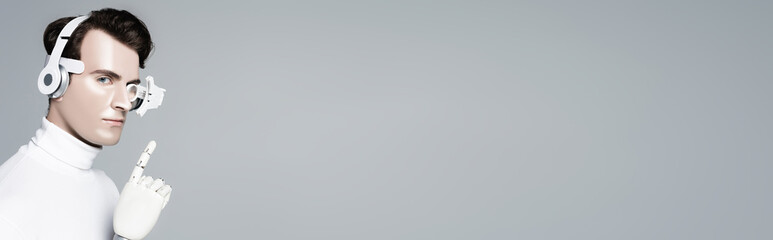 Cyborg in headphones and artificial hand pointing with finger isolated on grey, banner