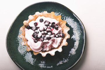 Photo of a tartlet with berries and whipped cream in a green plate over white background.
