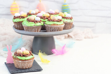 Easter carrot cake muffins with cream cheese frosting and chocolate eggs, on gray cake stand, horizontal, copy space