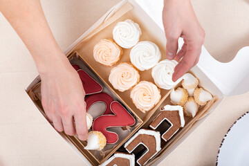 Female hands fill the Christmas box. Gingerbread, marshmallows in christmas box. Holiday baked goods