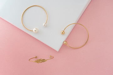 Three Modern golden bracelets on pink and white display