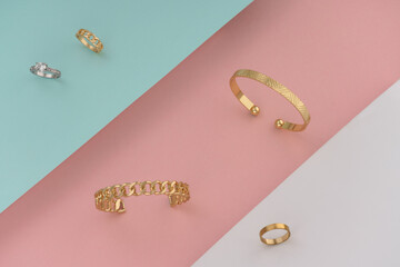 Golden accessories bracelets and rings on pastel colors background