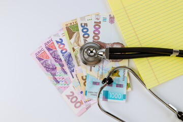 Stethoscope phonendoscope on a Ukrainian money grivna with banknotes on yellow notebook write in the white background
