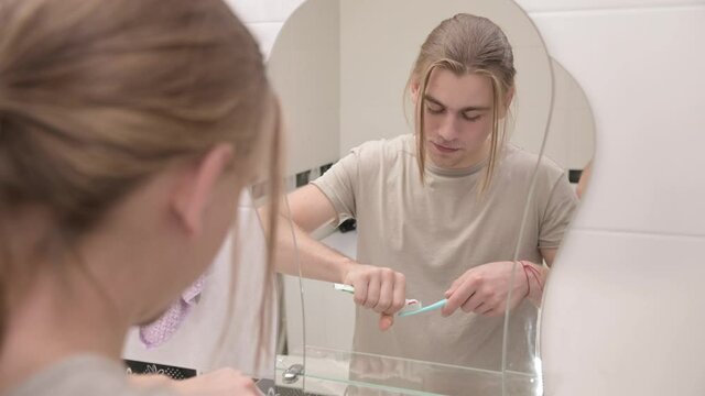 Young man in front of a mirror in the bathroom applies toothpaste to a toothbrush