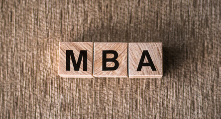 Fototapeta na wymiar MBA word written on wooden blocks on a brown background.