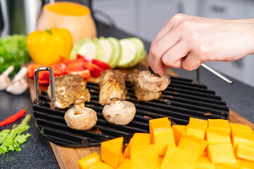 Female hand holds mushroom cooked on grill.