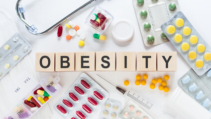 OBESITY medicine word on wooden blocks on a desk. Medical concept with pills, vitamins, stethoscope...