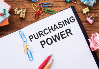 Notebook with text PURCHASING POWER on a table with sticks, colored paper clips and wrinkled sheets.