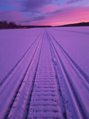 Trace of a snowmobile in the colorful frosty sunset with purple and pink colors.
