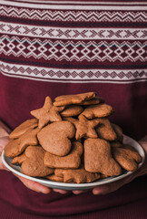 Homemade gingerbread cookies with orange zest in the hands of a male white man wearing a burgundy sweater with patterns. Homemade dessert.