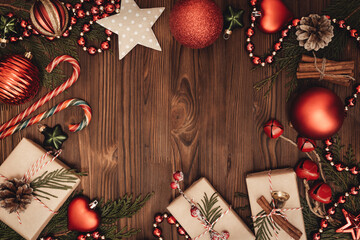 Christmas and New Year rustic traditional background with copy space. Festively decorated cedar branches on a dark brown old wooden board. Gift boxes, balls, stars and cane lollypops. Place for text.