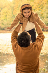Father and daughter dressed in autumn colors are having fun. Father held his daughter in the air. little girl laughing.