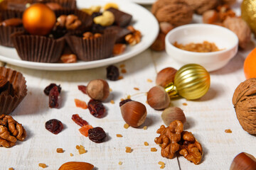 Fototapeta na wymiar sweet food background for christmas or holiday decoration - chocolate candies, tangerines, nuts and dried fruits on white wood
