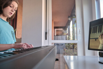 Caucasian Boy learning to play piano with video lessons. Concept of virtual learning