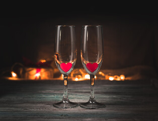 Romantic background with champagne glasses and hearts on the background of a burning garland in the dark. Side view, horizontal orientation. Concept of holiday backgrounds, love, February 14.