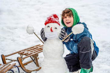 Happy boy is putting on a protective mask for a snowman. Sledding outdoors in the mountains the...