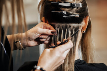 The hairdresser does hair extensions to a girl, a blonde in a beauty salon. Professional hair...