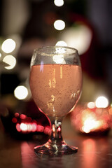 Festive rose fizzy drink in a transparent glass with blurred lights and candles background
