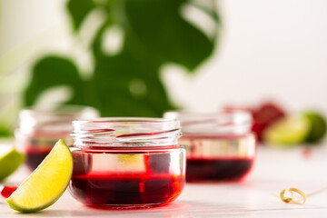 Red alcoholic shots on white background , small jars with liquor and grenadine with lime