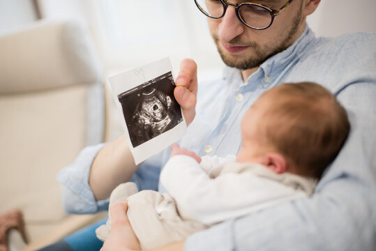 A man with a newborn baby showing an ultrasound picture, father moment with a baby