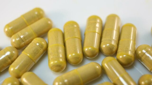 Yellow capsules on a white background move from right to left. Extreme close-up, real time, medicine, pharmacy, stabilization, camera movement