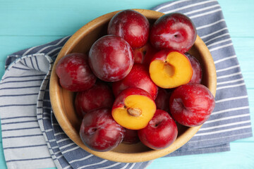 Delicious ripe plums in bowl on light blue wooden table, top view