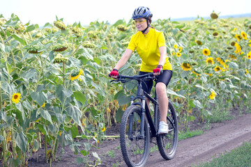 Beautiful woman cyclist rides a field with sunflowers on a bicycle. Healthy lifestyle and sport. Leisure and hobbies