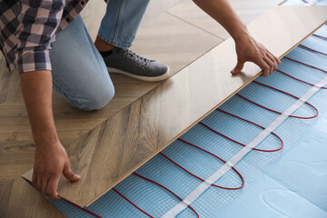 Professional contractor installing underfloor trace heating system indoors, closeup