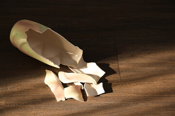 Broken ceramic vase on wooden floor, above view. Space for text