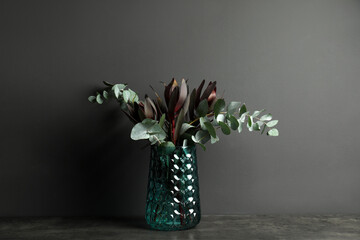 Bouquet of protea flowers and eucalyptus branches in glass vase on table against black background