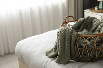 Knitted green plaid in wicker basket on bed indoors space for text.