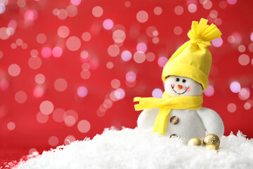 Snowman toy and Christmas balls on snow against blurred festive lights. Space for text
