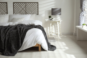Comfortable bed with warm knitted plaid in stylish room interior