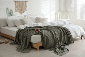 Comfortable bed with warm knitted plaid in stylish room interior