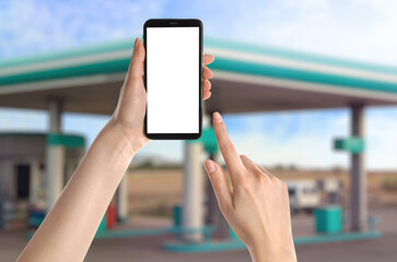 Woman paying for refueling via smartphone at gas station, closeup. Device with empty screen