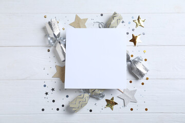 Flat lay composition of Christmas crackers, shiny confetti and blank paper on white wooden...