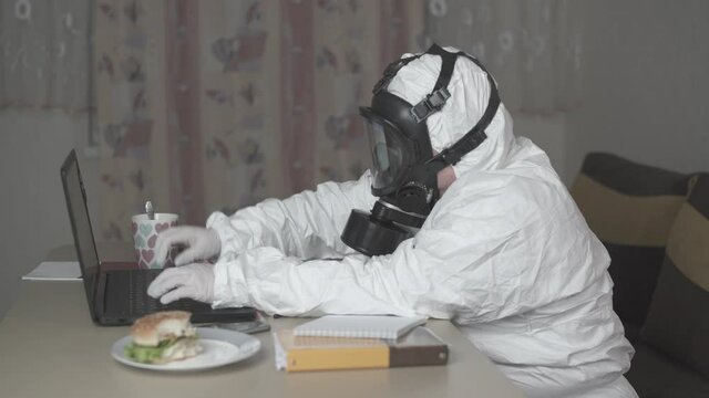 Fat woman in gas mask and protective suit working at her desk in her home office. Typing and writing.