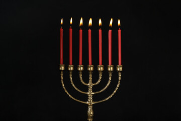 Golden menorah with burning candles on black background