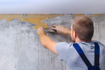 A man removes old wallpaper with a spatula and a spray bottle with water.